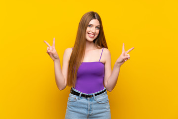 Young woman over isolated yellow background showing victory sign with both hands