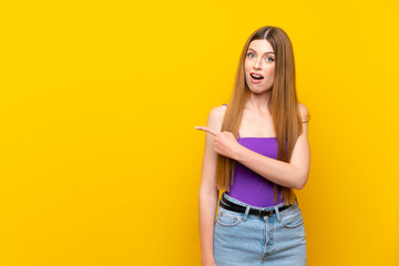 Young woman over isolated yellow background surprised and pointing side