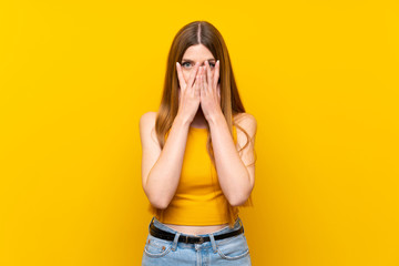 Young woman over isolated yellow background covering eyes and looking through fingers
