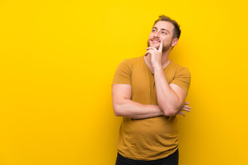 Blonde man over isolated yellow wall thinking an idea while looking up