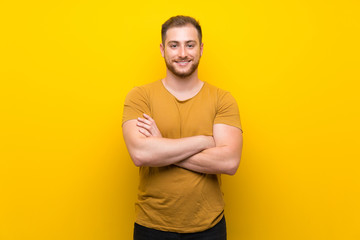 Blonde man over isolated yellow wall keeping the arms crossed in frontal position