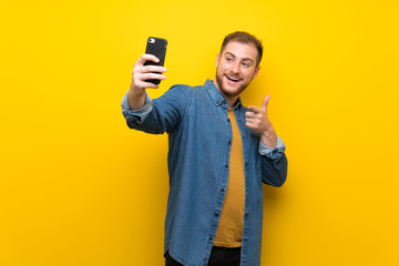 Blonde man over isolated yellow wall making a selfie