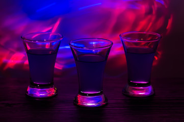 Three drinks at the party. Three shots with cocktails at the bar. Liquor, vodka, fresh. Shining on a colored background. Night club, after  party.
