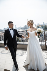 A groom and a bride are looking at each other while walking on a terrace.