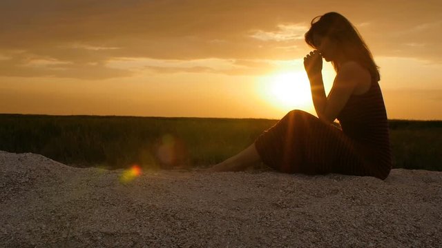 silhouette of a young woman on the sand at sunset, girl bowed her head in prayer to the Creator with gratitude, the concept of rest, religion, the beauty of nature and harmony