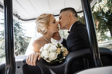Newlyweds are kissing in a golf car.