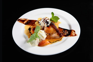 Peach flambe with ice cream balls on a plate. Great dessert on a plate on a black background. Macro photo. The concept of high cuisine.