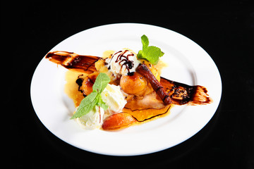 Peach flambe with ice cream balls on a plate. Great dessert on a plate on a black background. Macro photo. The concept of high cuisine.