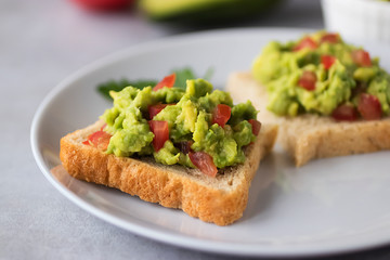Toasts with an avocado snack and fresh vegetables on a gray background.