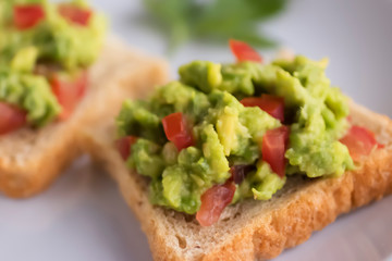 Toasts with an avocado snack and fresh vegetables on a gray background.