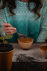 Woman wating a passion fruit mousse with passion fruit seeds and a seedling of passion fruit tree in the scene inside a coffee mug, with a dark background