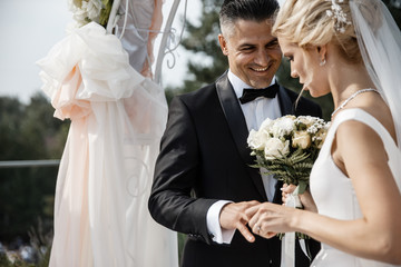 A bride and a groom are putting the rings on each others fingers.