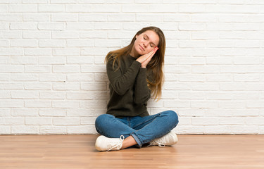 Young woman sitting on the floor making sleep gesture in dorable expression