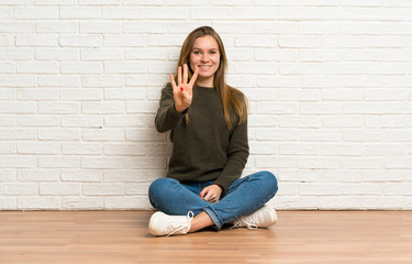 Young woman sitting on the floor happy and counting four with fingers
