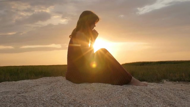silhouette of a young woman on the sand at sunset, girl bowed her head in prayer to the Creator with gratitude, the concept of rest, religion, the beauty of nature and harmony