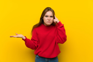 Young woman over yellow wall making the gesture of madness putting finger on the head