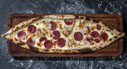 Traditional Turkish pide aka Turkish pizza with kashar cheese and Turkish sausage on wooden cut board on a black floor full of flour 