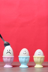 A boiled egg with a chopped shell stands in a poached. On the egg painted smiley. A spoon is stuck in it for food. Against the background of coral color.