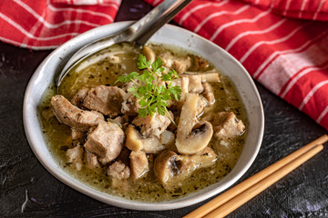 Soup with pieces of pork and mushrooms in bowl.