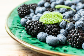 Fresh organic blackberries and blueberries on green ceramic plate close up.
