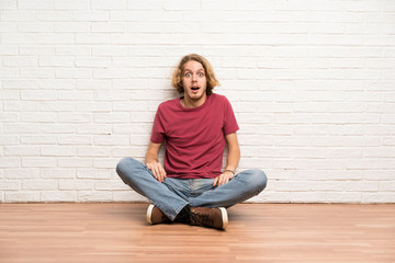 Blonde man sitting on the floor with surprise facial expression