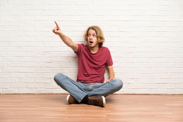 Blonde man sitting on the floor pointing away