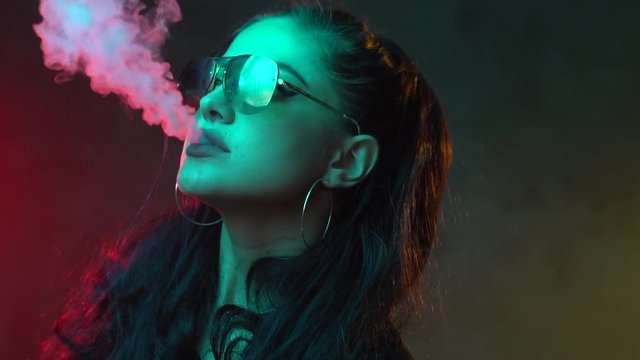 Gorgeous brunette woman smoking electronic cigarette in neon color light - video in slow motion