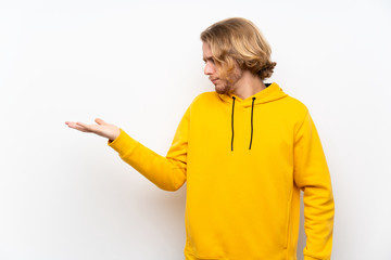 Blonde man with  sweatshirt over white wall holding copyspace with doubts