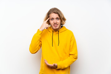 Blonde man with  sweatshirt over white wall making the gesture of madness putting finger on the head