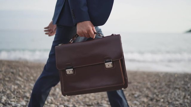 Businessman is walking by the sea shore in formal suit with briefcase