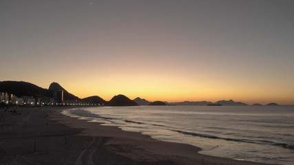 Fototapeta na wymiar Aerial view of Copacabana beach early in the morning before sunrise at golden hour with waves rolling in, city lights, Sugarloaf mountain and hills of Niteroi in the background