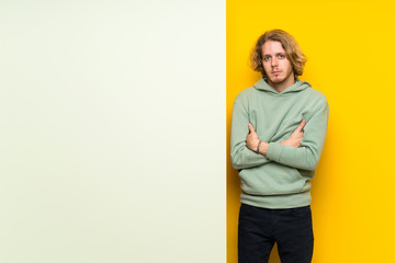 Blonde man holding a big empty placard keeping arms crossed