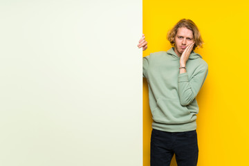 Blonde man holding a big empty placard unhappy and frustrated