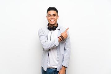 Fototapeta premium Young man over isolated white wall with earphones pointing to the side to present a product