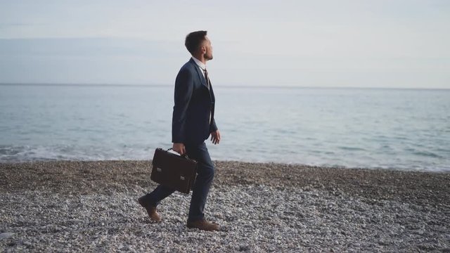 Businessman is walking by the sea shore in formal suit with briefcase