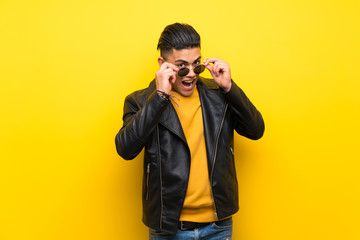 Young man over isolated yellow background with glasses and surprised
