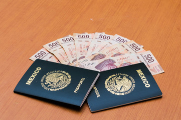 Dos pasaportes mexicanos apilados. Un paquete de billetes de quinientos pesos mexicanos dispuestos como un abanico en una mesa de madera. Pesos mexicanos en efectivo. Concepto de viajes y turismo.