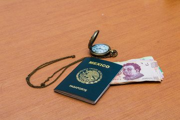 Reloj de bolsillo junto al pasaporte mexicano. Un paquete de billetes de quinientos pesos mexicanos dispuestos como un abanico en una mesa de madera. Pesos mexicanos en efectivo. Concepto de viajes