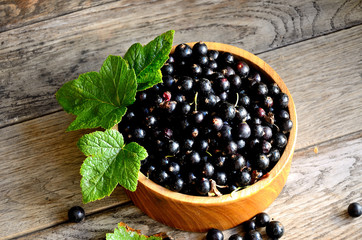 Black currant in a wooden bowl on the background of old boards, top view.