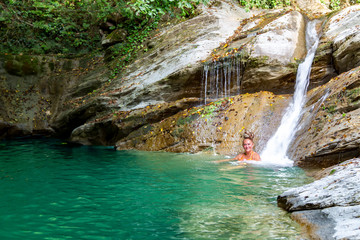 Pretty woman bathes in a mountain lake with waterfalls in the gorge Ahtsu area of Sochi, Russia.