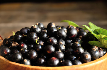 Harvest, ripe black currants, in a wooden bowl on old wooden boards.
