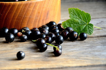 Harvest, ripe black currants, in a wooden bowl on old wooden boards.