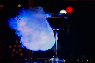 Photo of a glass with a cocktail and smoke with light, shot on a bar with a dark background