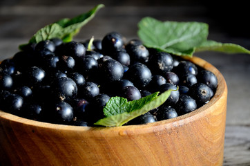 Harvest, ripe black currants, in a wooden bowl on old wooden boards.