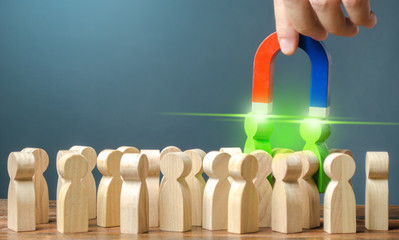 Businessman with a magnet pulls two green figures of people out of the crowd. Recruiting new...