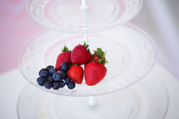 Beautiful strawberries and blueberries on a crystal saucer on a pink background