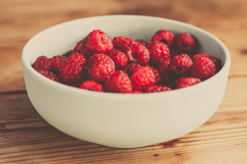 Fresh raspberries background closeup photo. Red raspberries in bowl on wooden table. Vintage style