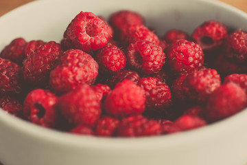 Fresh raspberries background closeup photo. Red raspberries in bowl on wooden table. Vintage style