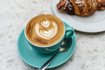 Top view of cup of coffee with foam and croissant on the table.