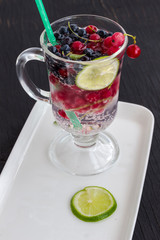Glass with a cooling drink of berries and ice. Misted glass. A slice of lemon on a plate